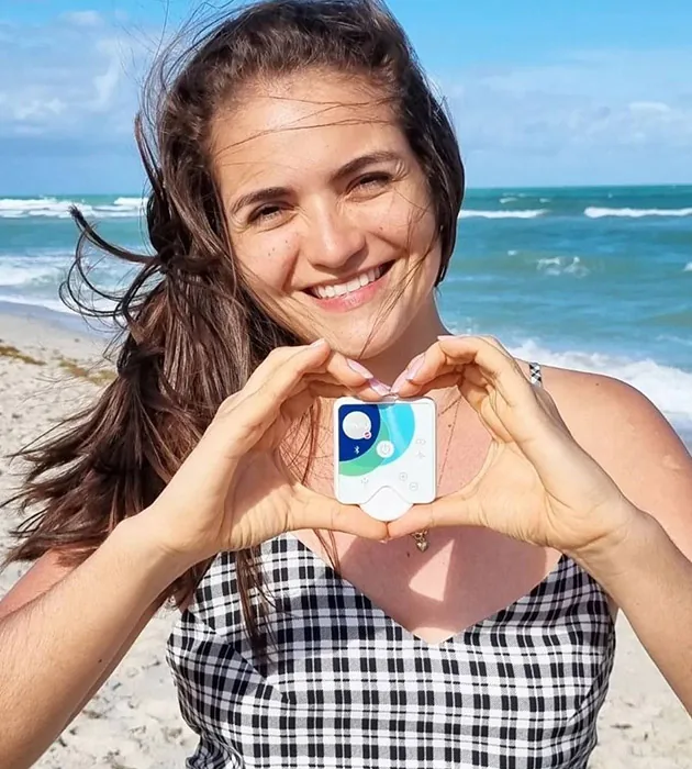 A smiling woman on a beach holding Healy in a heart shape with her hands